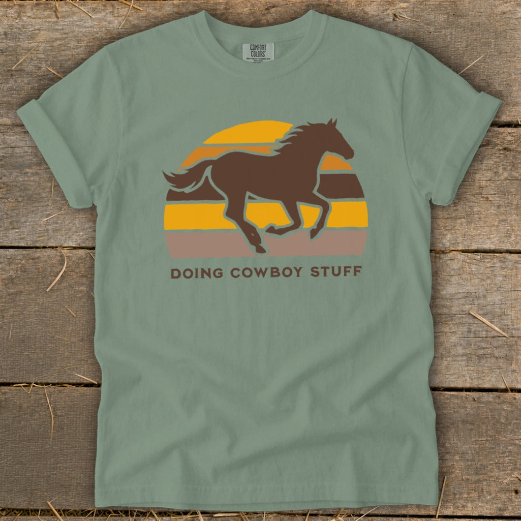 Green t-shirt with brown horse and sunset graphic. "Doing Cowboy Stuff" text.