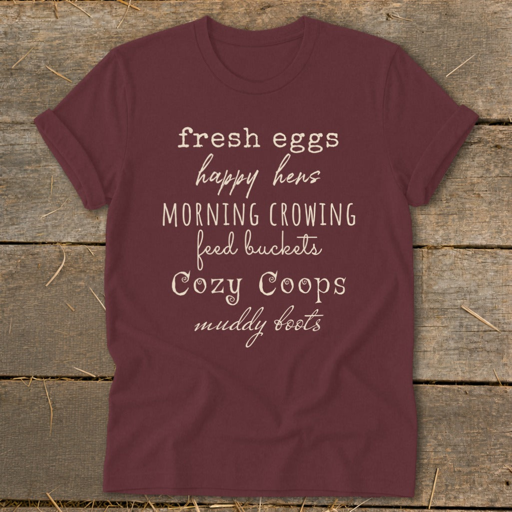 Maroon t-shirt with white text: fresh eggs, happy hens, MORNING CROWING, feed buckets, Cozy Coops, muddy boots.