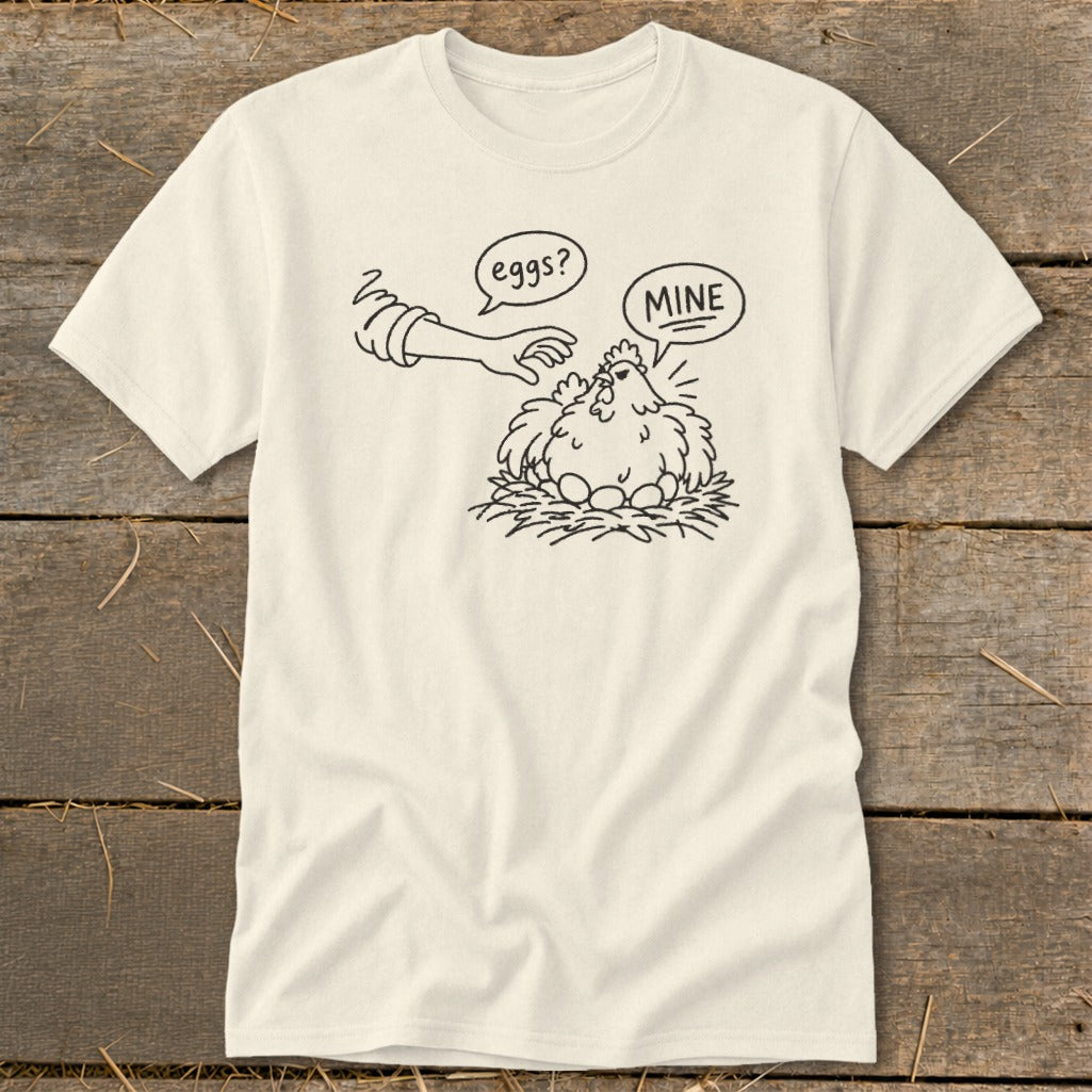 Cream t-shirt with cartoon chicken saying "MINE" to a hand reaching for eggs.