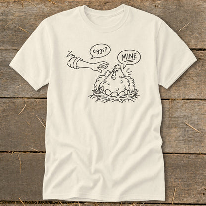 Cream t-shirt with cartoon chicken saying "MINE" to a hand reaching for eggs.