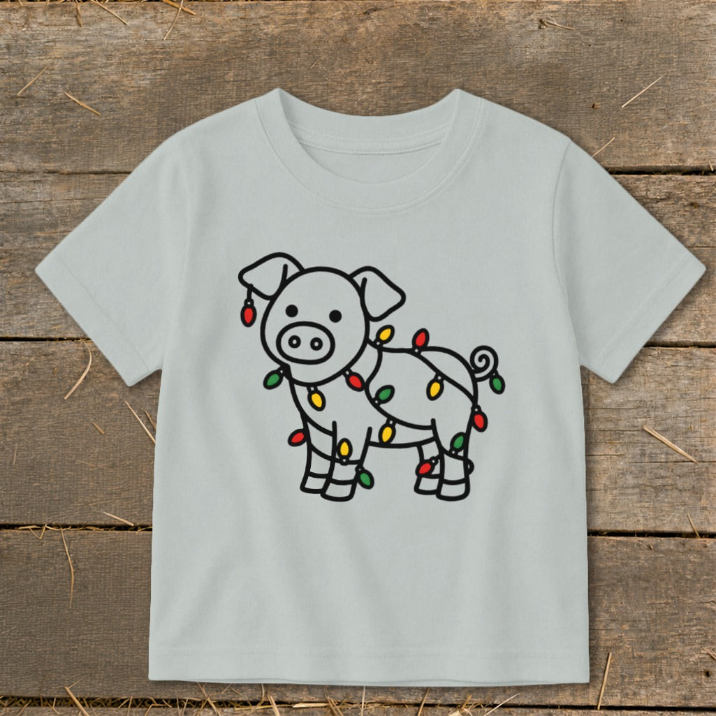 A light gray children's t-shirt features a cartoon pig wrapped in colorful Christmas lights.
