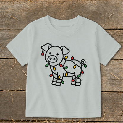 A light gray children's t-shirt features a cartoon pig wrapped in colorful Christmas lights.