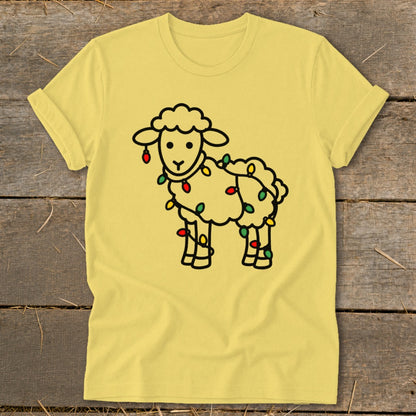 Yellow short-sleeve t-shirt featuring a cartoon sheep tangled in colorful Christmas lights, laid flat on a rustic wooden background.
