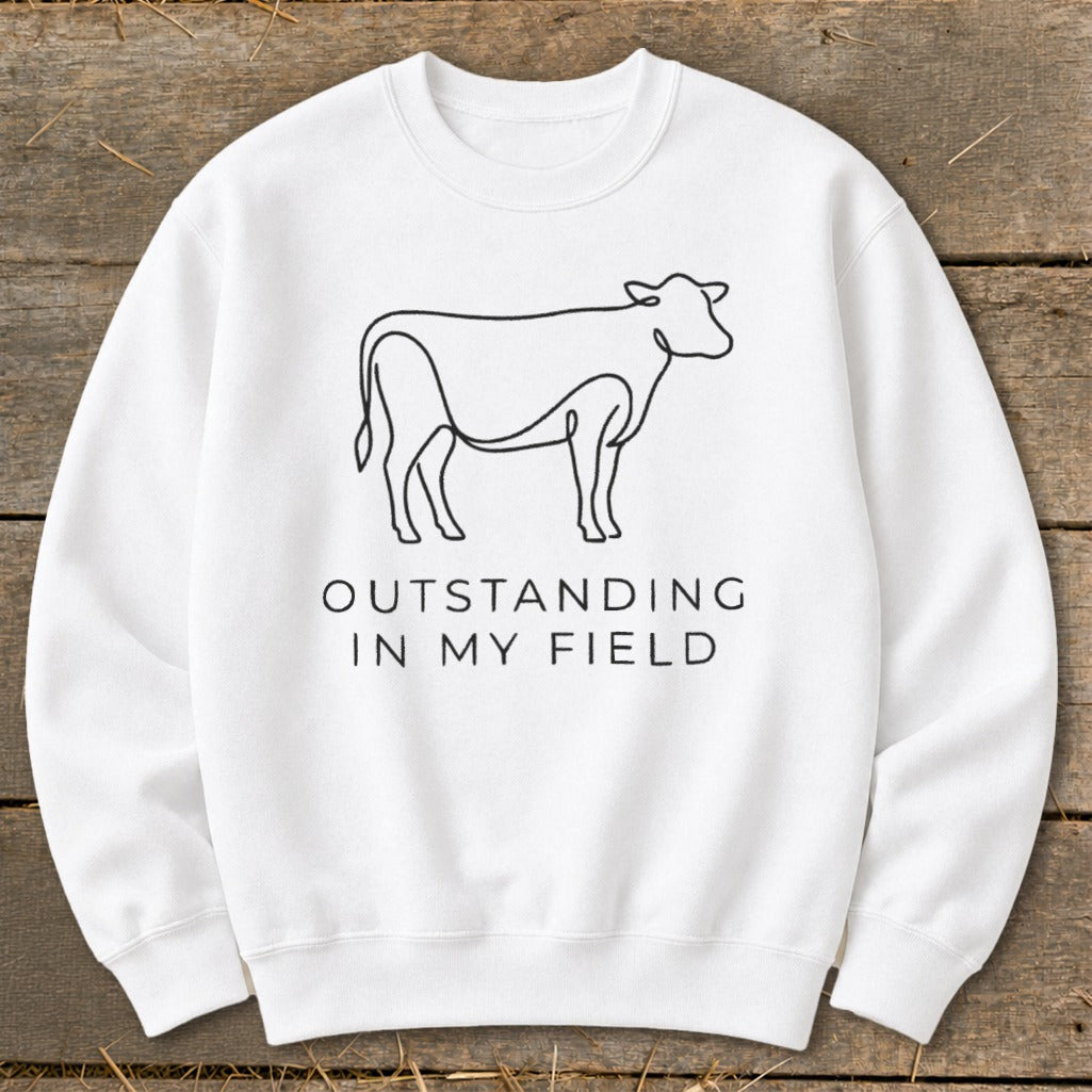 White sweatshirt with black line drawing of a cow and text "OUTSTANDING IN MY FIELD".