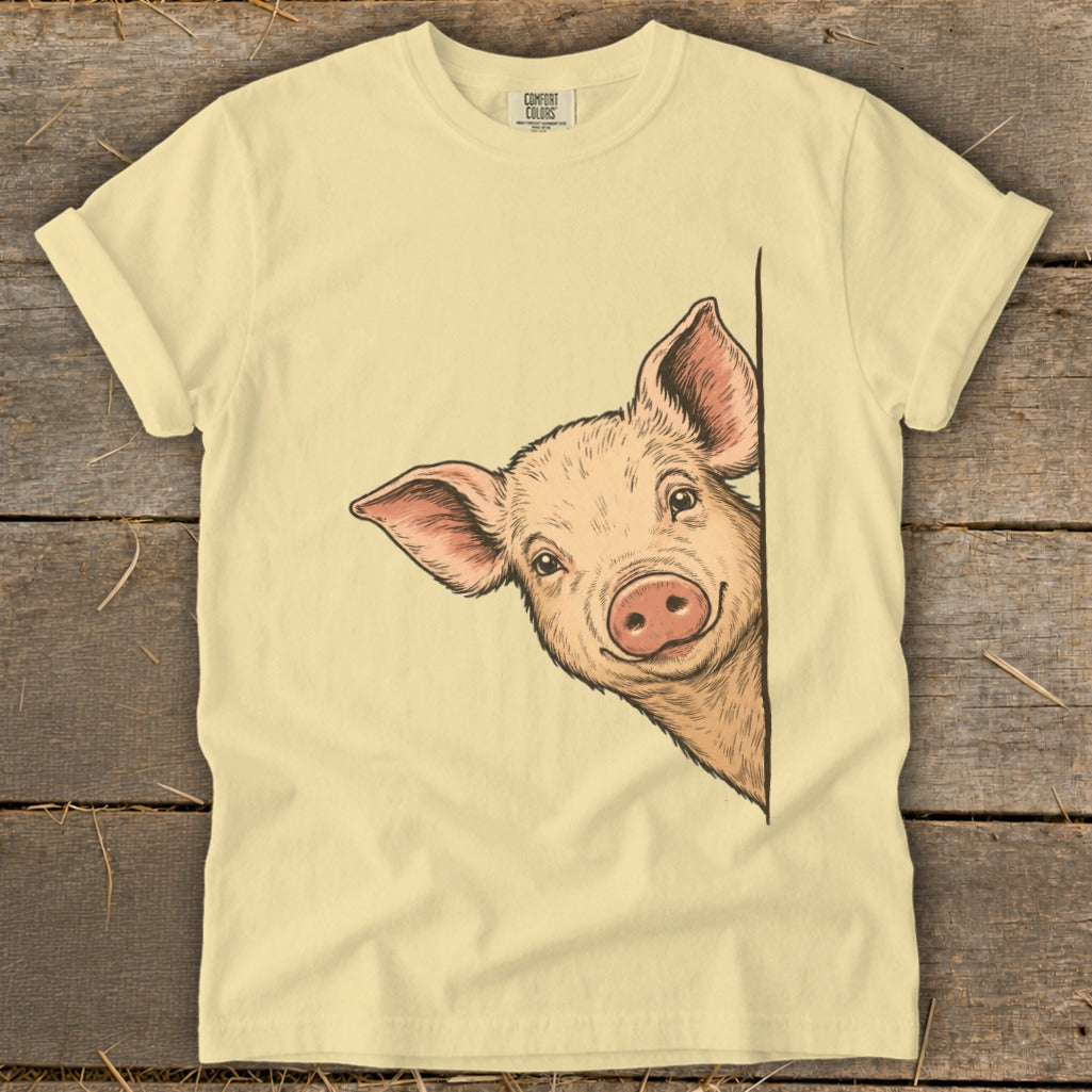 Light yellow t-shirt with a drawing of a smiling pig peeking from the side.