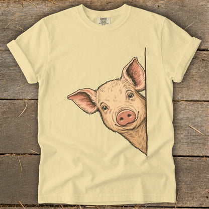 Light yellow t-shirt with a drawing of a smiling pig peeking from the side.