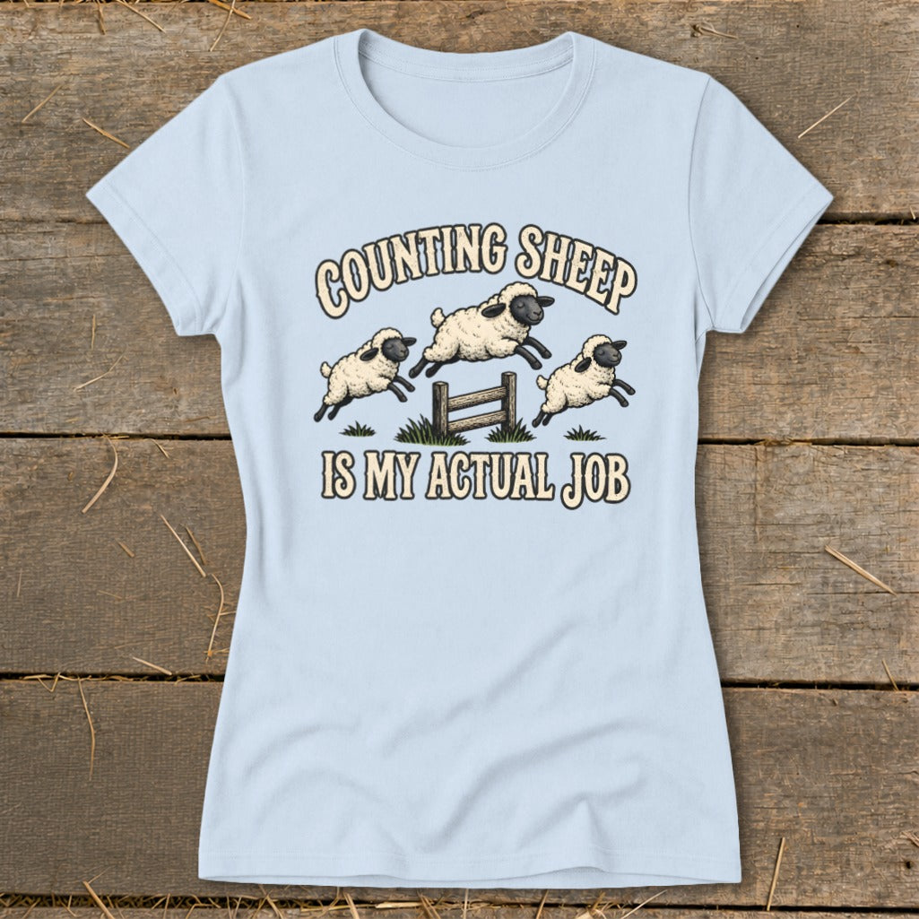 Light blue t-shirt with cartoon sheep jumping over a fence with text "COUNTING SHEEP IS MY ACTUAL JOB".