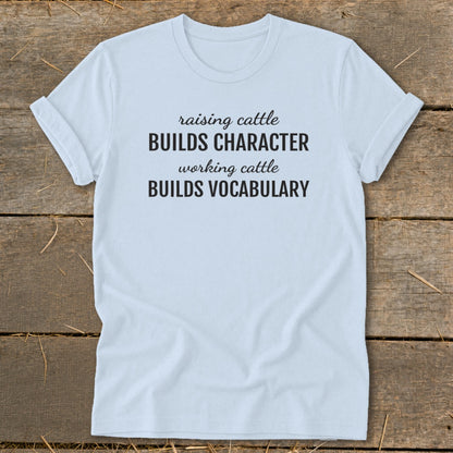 Light blue t-shirt with black text reading "raising cattle BUILDS CHARACTER working cattle BUILDS VOCABULARY".