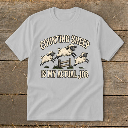 Light grey t-shirt with "COUNTING SHEEP IS MY ACTUAL JOB" and jumping sheep graphic.