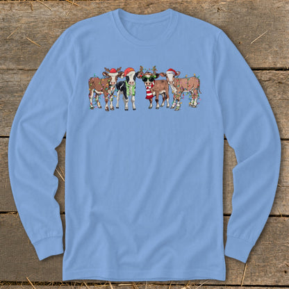 Cartoon cows in festive Christmas hats and lights on a light blue long-sleeve shirt.