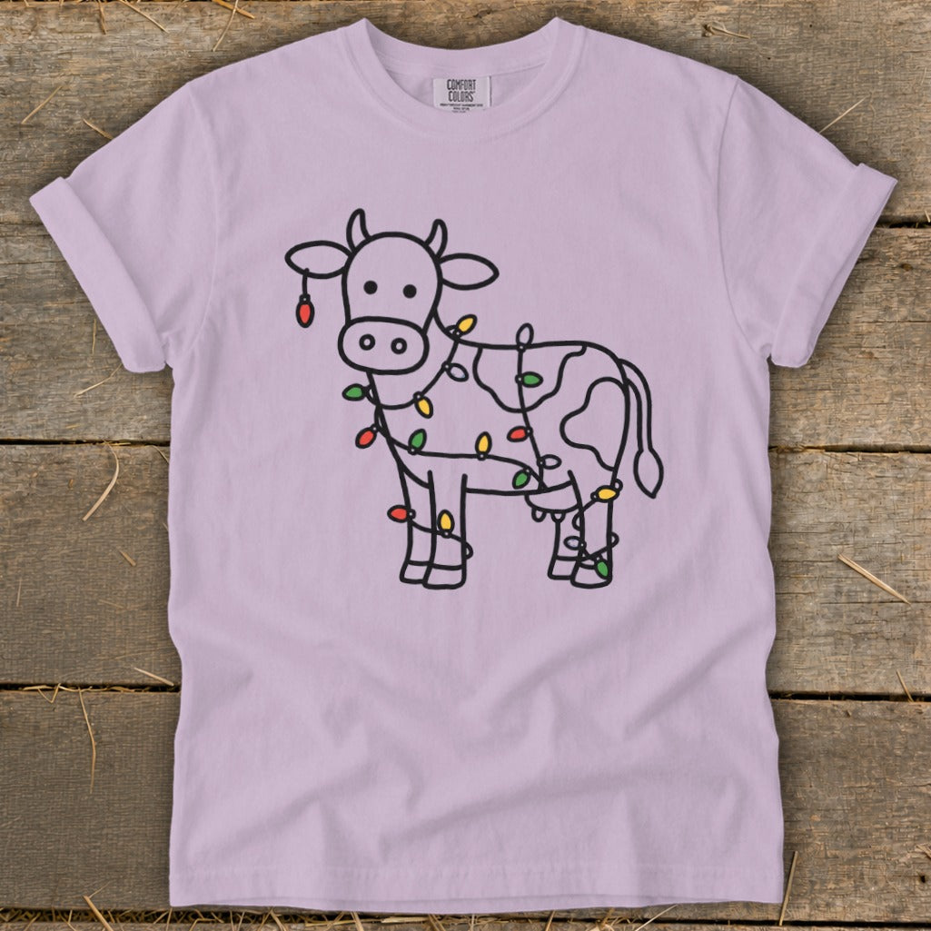 Light purple t-shirt with a black outline drawing of a cow wrapped in colorful Christmas lights.