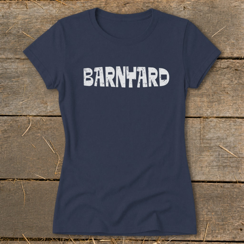A dark blue women's t-shirt laid flat on a wooden background, featuring the distressed white text "BARNYARD" across the chest.