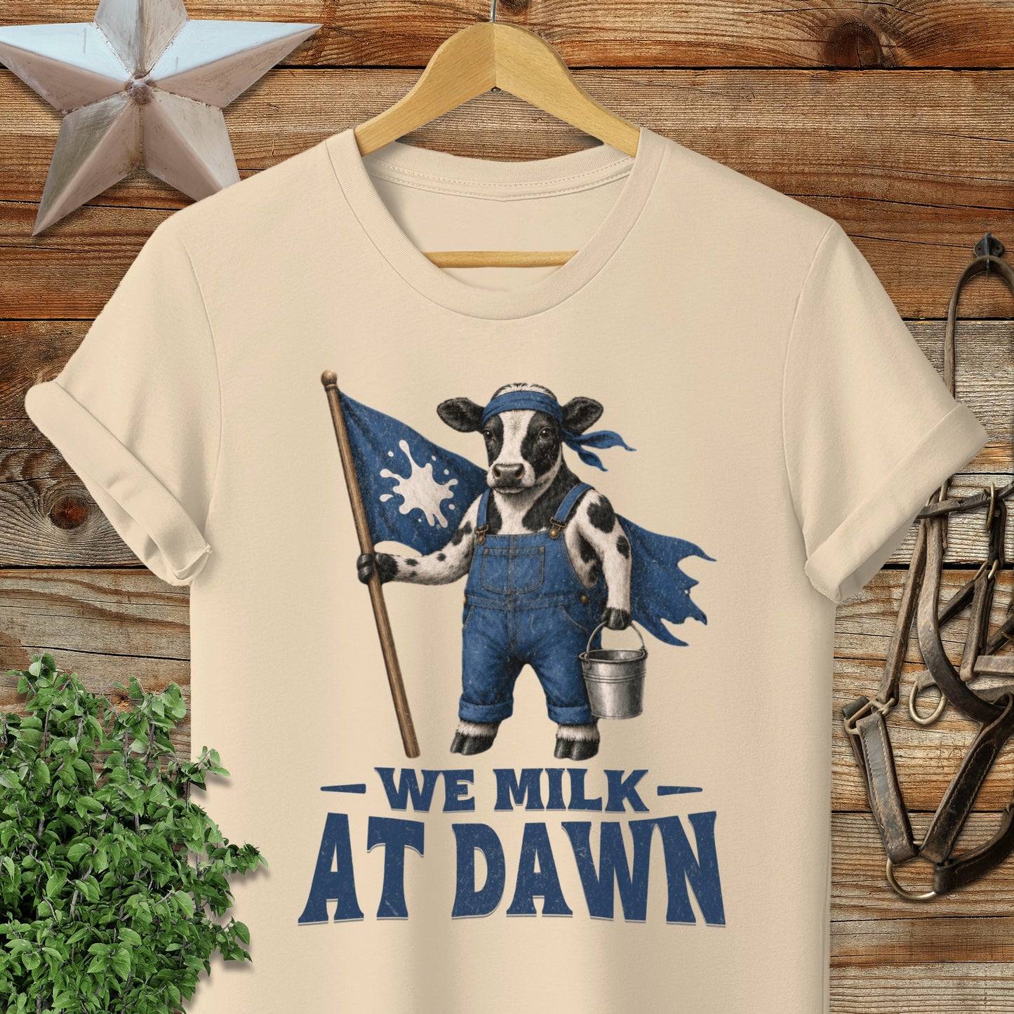 Cow in overalls holding a flag and milk bucket with text "We Milk At Dawn".