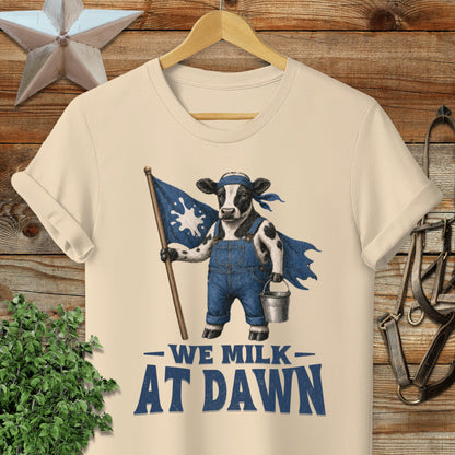 Cow in overalls holding a flag and milk bucket with text "We Milk At Dawn".