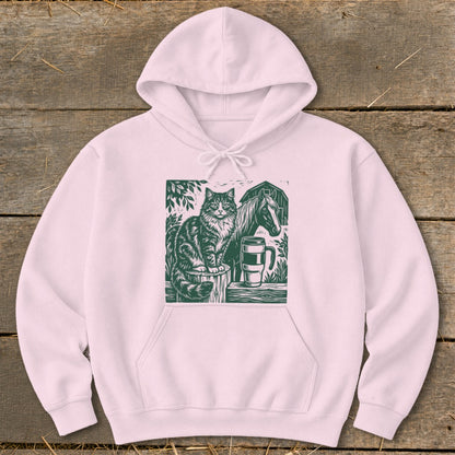 Pink hoodie with a green woodcut print of a cat, horse, barn, and mug.