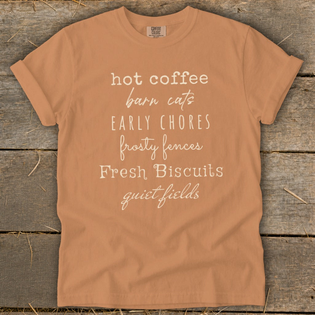 Orange t-shirt with text listing "hot coffee, barn cats, early chores, frosty fences, fresh biscuits, quiet fields."