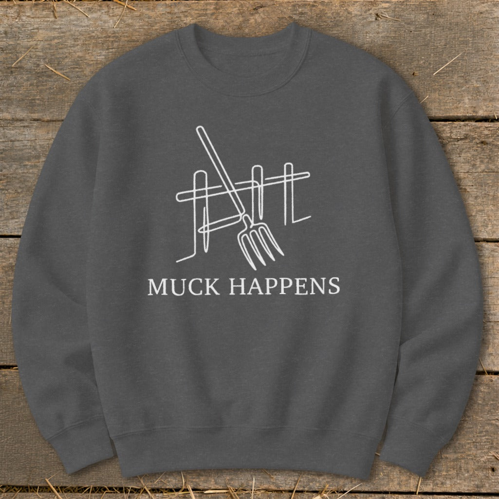 Charcoal sweatshirt with white line art of pitchfork and fence, text "MUCK HAPPENS".