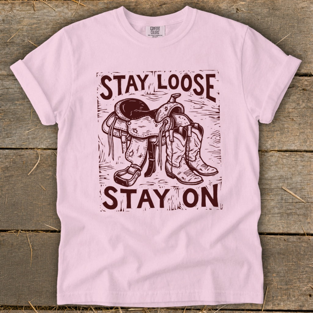 Pink t-shirt with maroon graphic of saddle and boots and text "STAY LOOSE STAY ON".