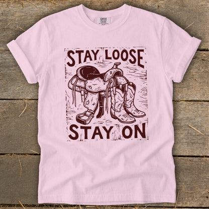 Pink t-shirt with maroon graphic of saddle and boots and text "STAY LOOSE STAY ON".