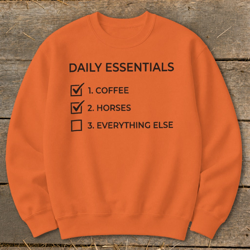 Orange crewneck sweatshirt with "Daily Essentials" checklist: Coffee, Horses, Everything Else.