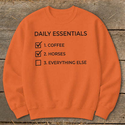 Orange crewneck sweatshirt with "Daily Essentials" checklist: Coffee, Horses, Everything Else.