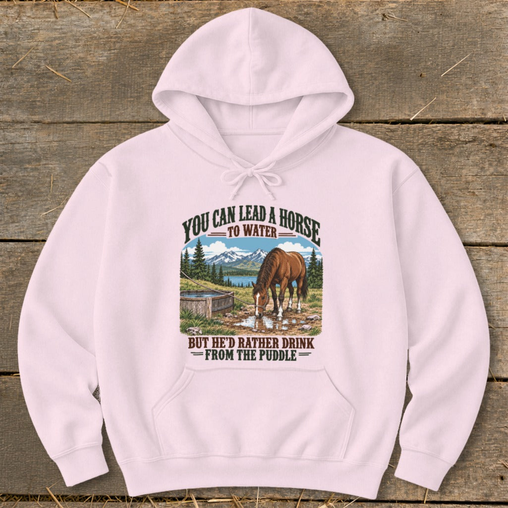 A light pink hooded sweatshirt features a graphic of a horse drinking from a puddle with mountain scenery.