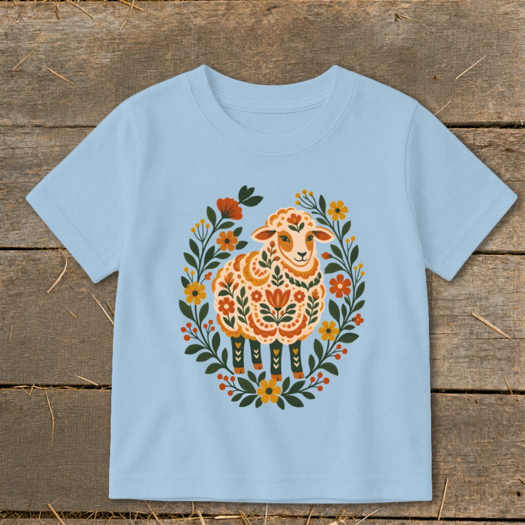 Light blue t-shirt with a folk art sheep illustration surrounded by flowers.
