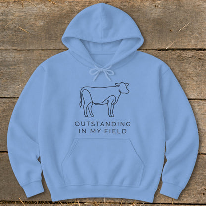 Light blue hoodie with line art cow and "OUTSTANDING IN MY FIELD" text.