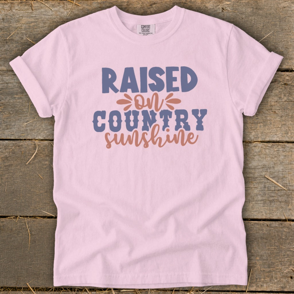 Pink t-shirt with text "Raised on Country Sunshine" in blue and coral.