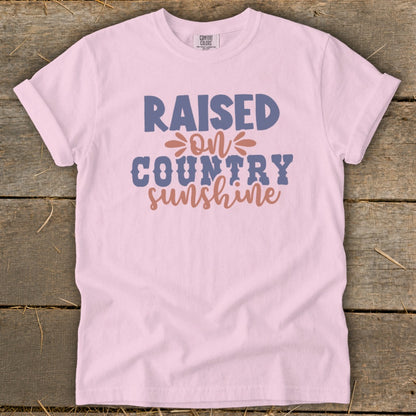 Pink t-shirt with text "Raised on Country Sunshine" in blue and coral.