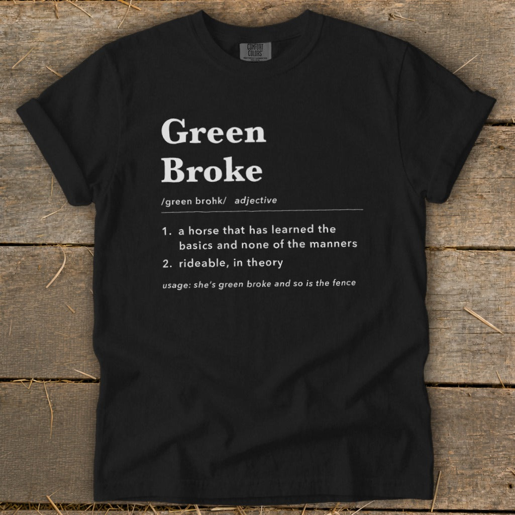Black t-shirt featuring dictionary-style text defining Green Broke laid flat on wooden planks.