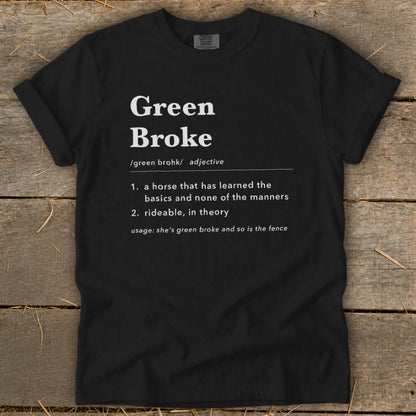 Black t-shirt featuring dictionary-style text defining Green Broke laid flat on wooden planks.