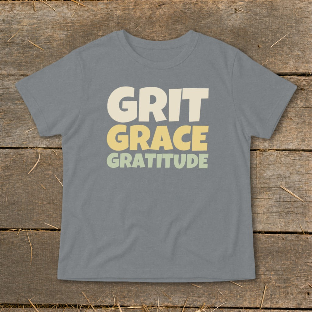 A gray short-sleeve t-shirt features the words "GRIT," "GRACE," and "GRATITUDE" printed in stacked, block lettering.