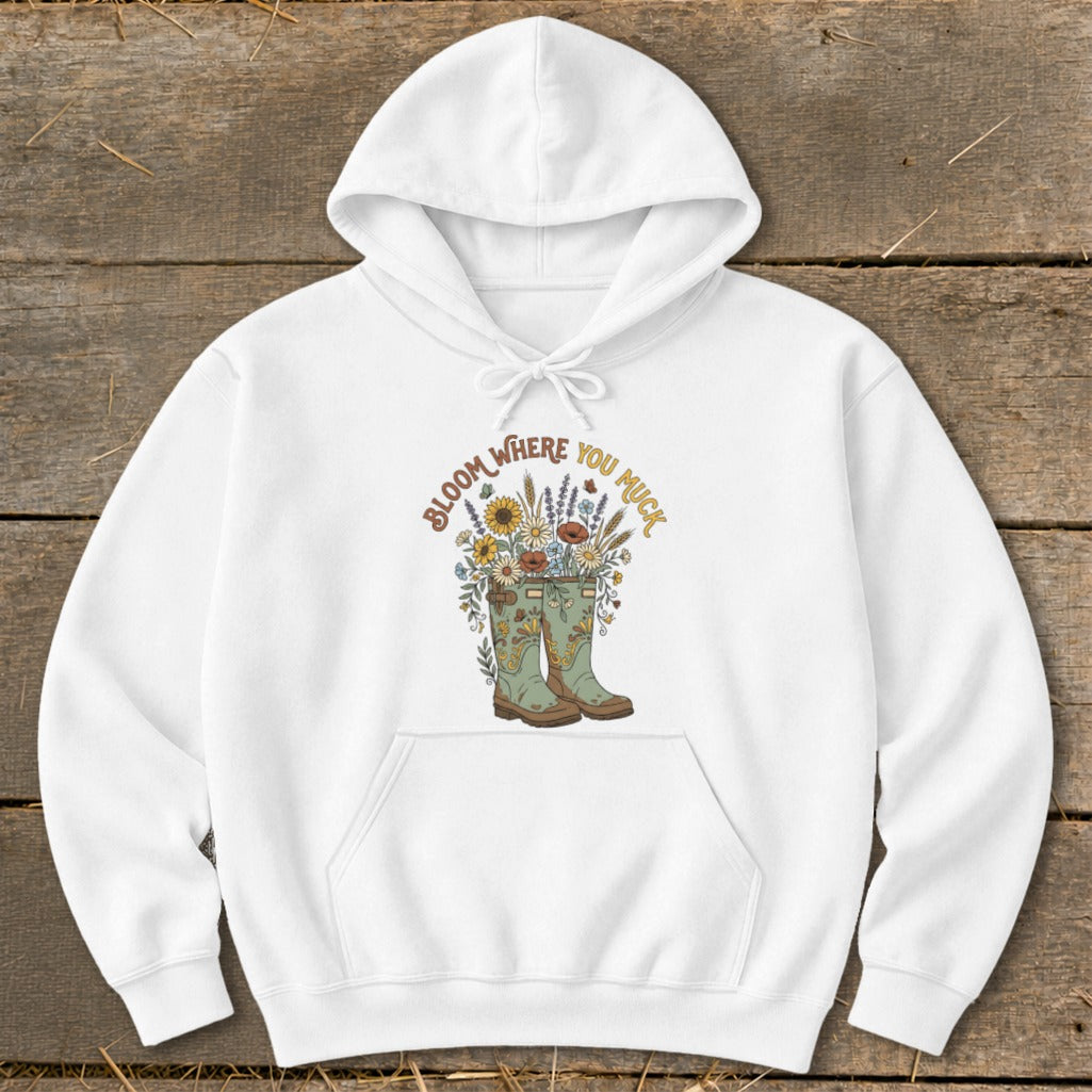White hoodie with graphic of boots overflowing with flowers and text "Bloom Where You Muck."