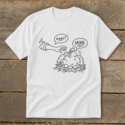 White t-shirt with cartoon hen protecting eggs, hand reaching for eggs, text "eggs?" and "MINE".