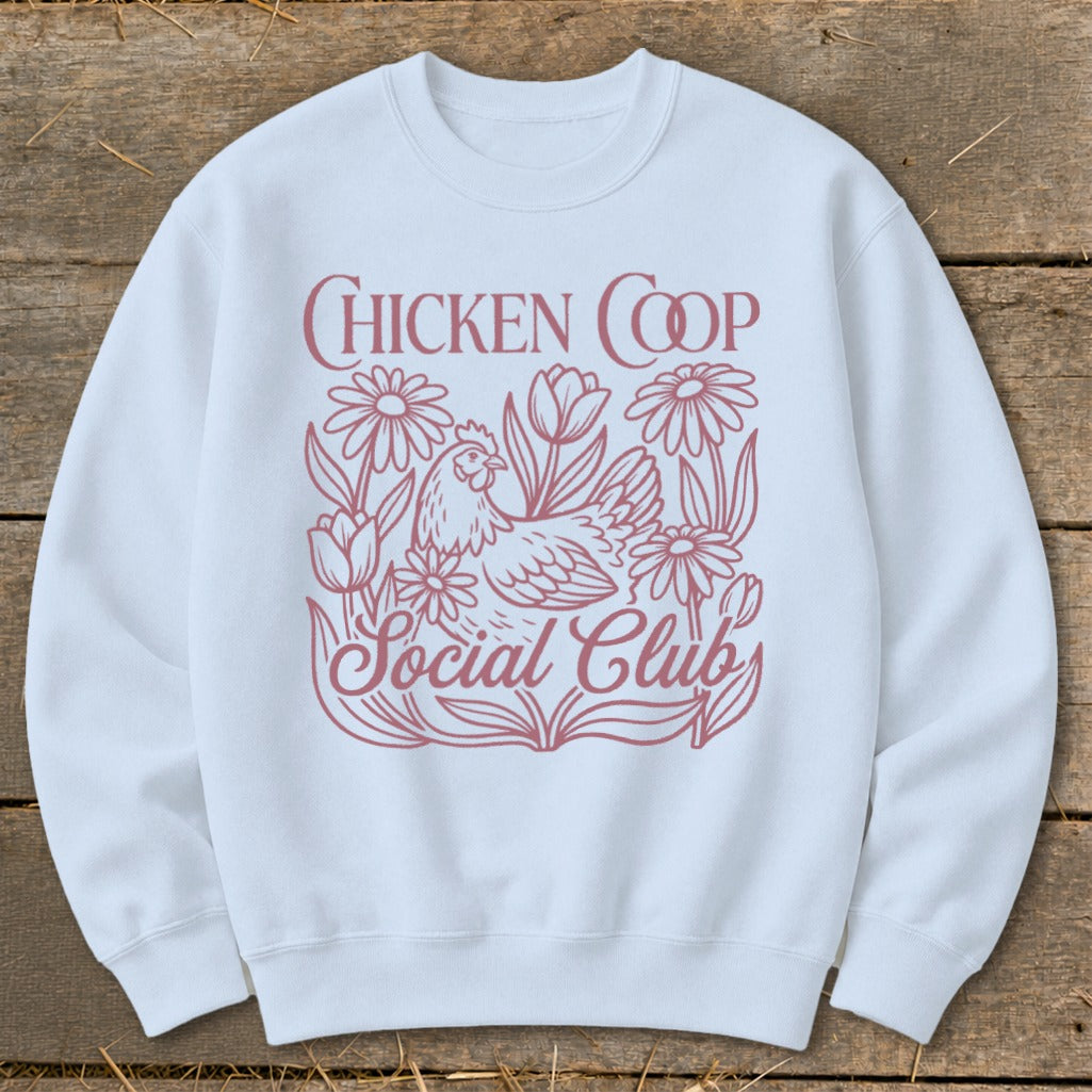 White sweatshirt with a pink graphic of a chicken surrounded by flowers and the text "Chicken Coop Social Club".