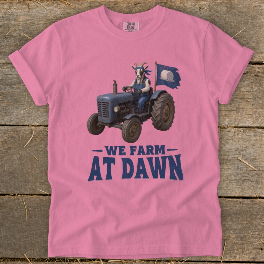 Pink t-shirt with a goat driving a tractor and the text "WE FARM AT DAWN".