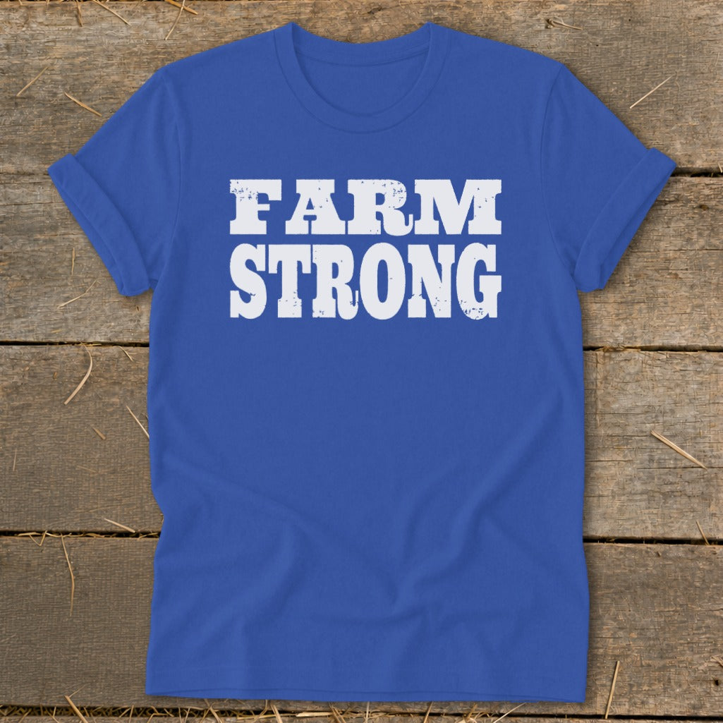 Royal blue t-shirt featuring white distressed text that reads FARM STRONG, laid flat on a rustic wooden surface.