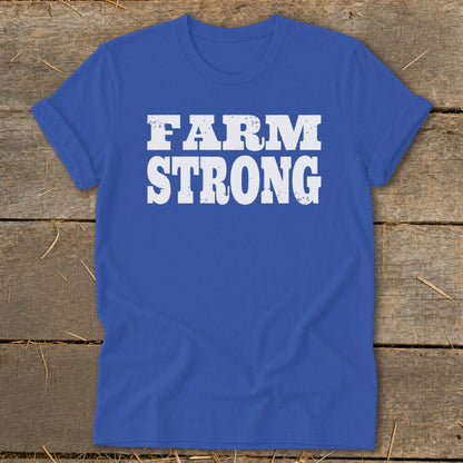 Royal blue t-shirt featuring white distressed text that reads FARM STRONG, laid flat on a rustic wooden surface.