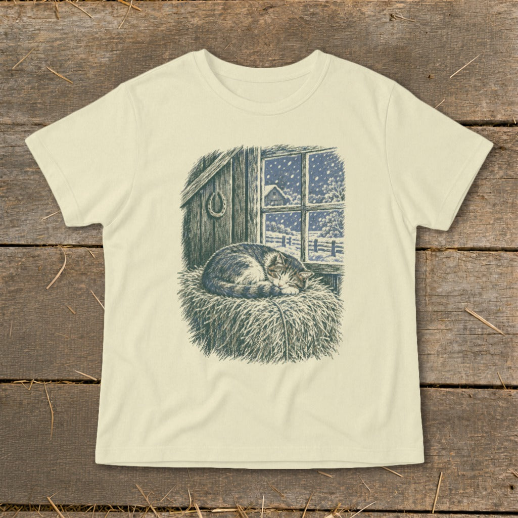 T-shirt graphic of a cat sleeping on hay by a window with snow falling.