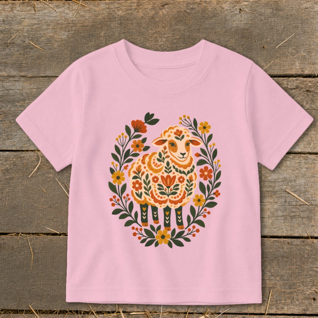 Pink t-shirt with a folk art sheep surrounded by a floral wreath.
