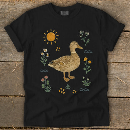 Black t-shirt with a duck surrounded by flowers, sun, and water elements.
