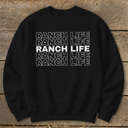 Black crewneck sweatshirt featuring stacked white text that reads "RANCH LIFE" laid flat on a rustic wooden surface.