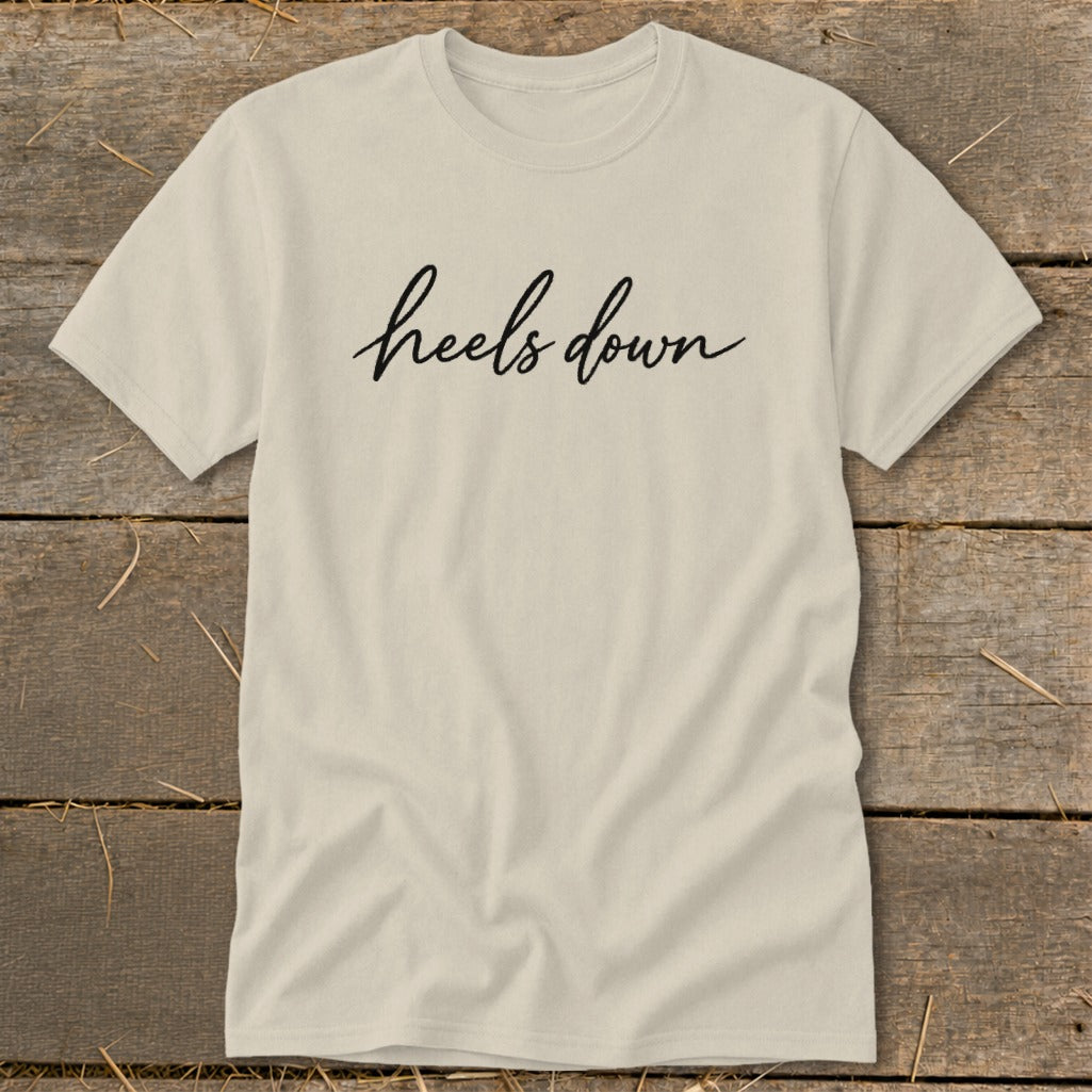 Cream t-shirt with black cursive text that reads "heels down".