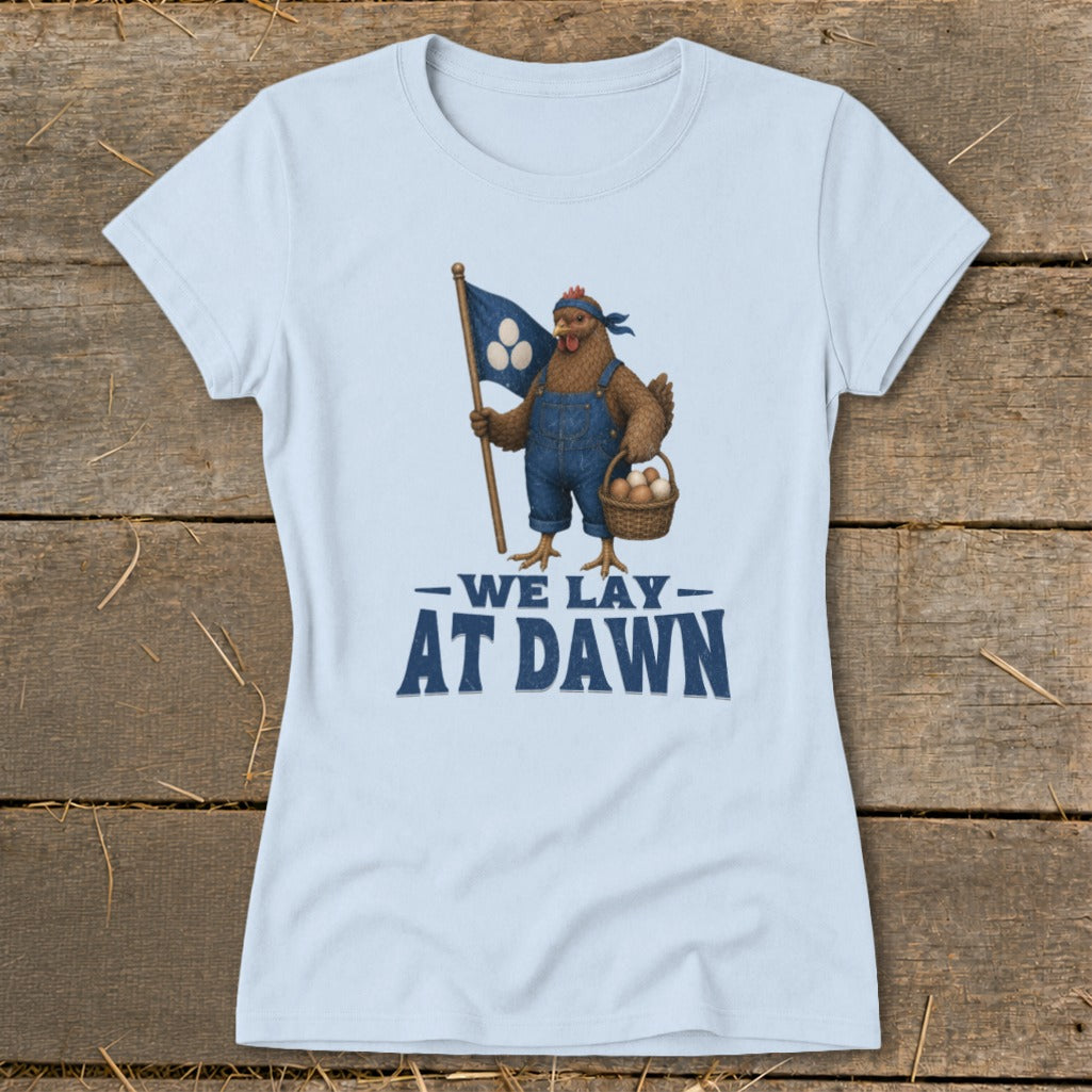 Light blue t-shirt with a cartoon chicken holding a flag and a basket of eggs. Text reads "We Lay At Dawn".