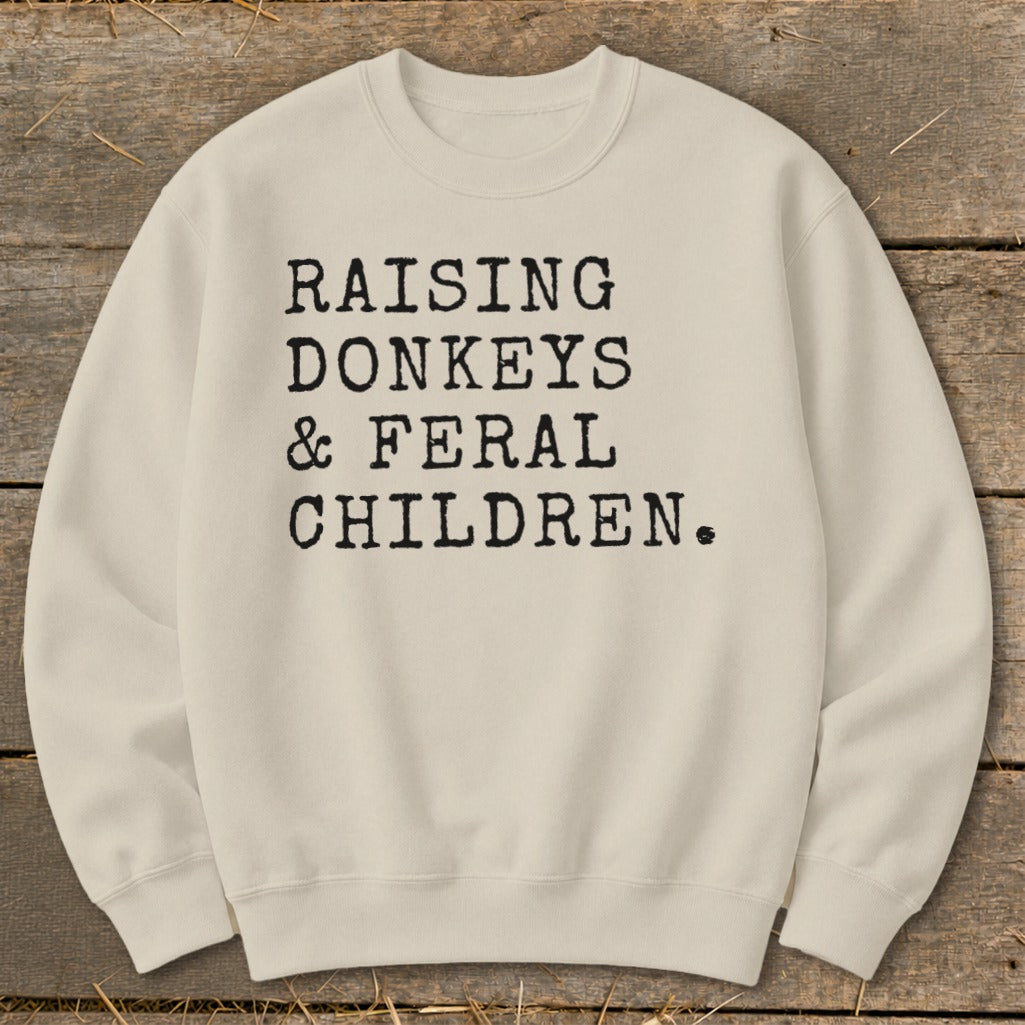 Cream sweatshirt with black text: Raising Donkeys & Feral Children.