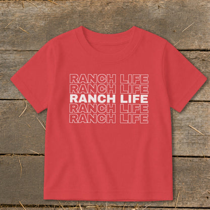 A red t-shirt printed with the text RANCH LIFE lies flat on a wooden surface.