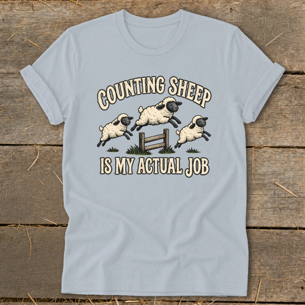 Light blue t-shirt with three cartoon sheep jumping over a fence, text says "COUNTING SHEEP IS MY ACTUAL JOB".