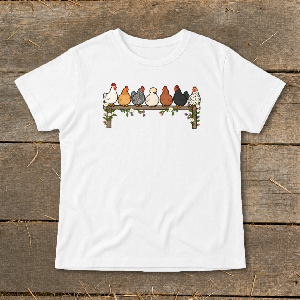 A white short-sleeved t-shirt features an illustration of seven colorful chickens perched on a floral fence.