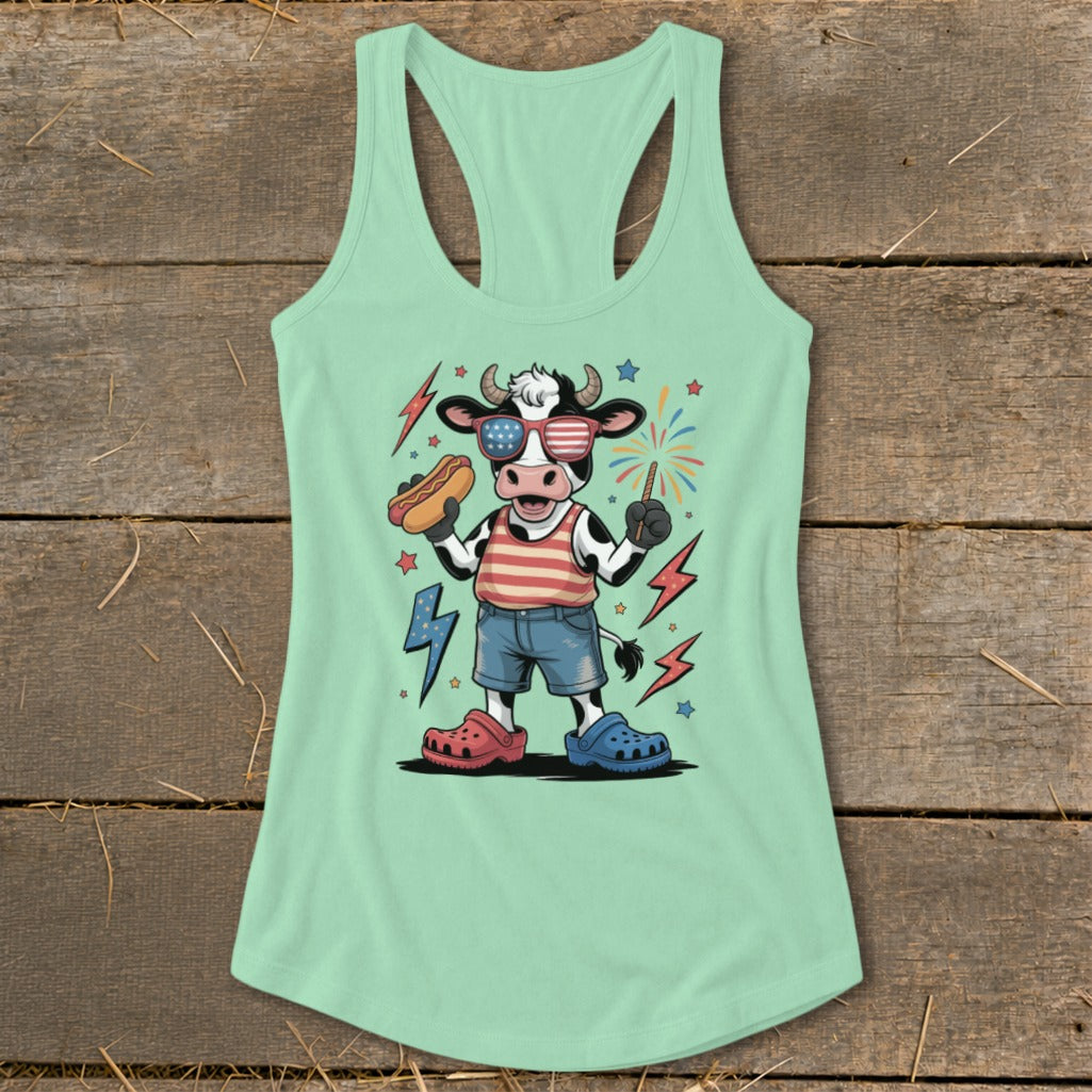 Cow with hot dog and sparkler on light green tank top with fireworks.